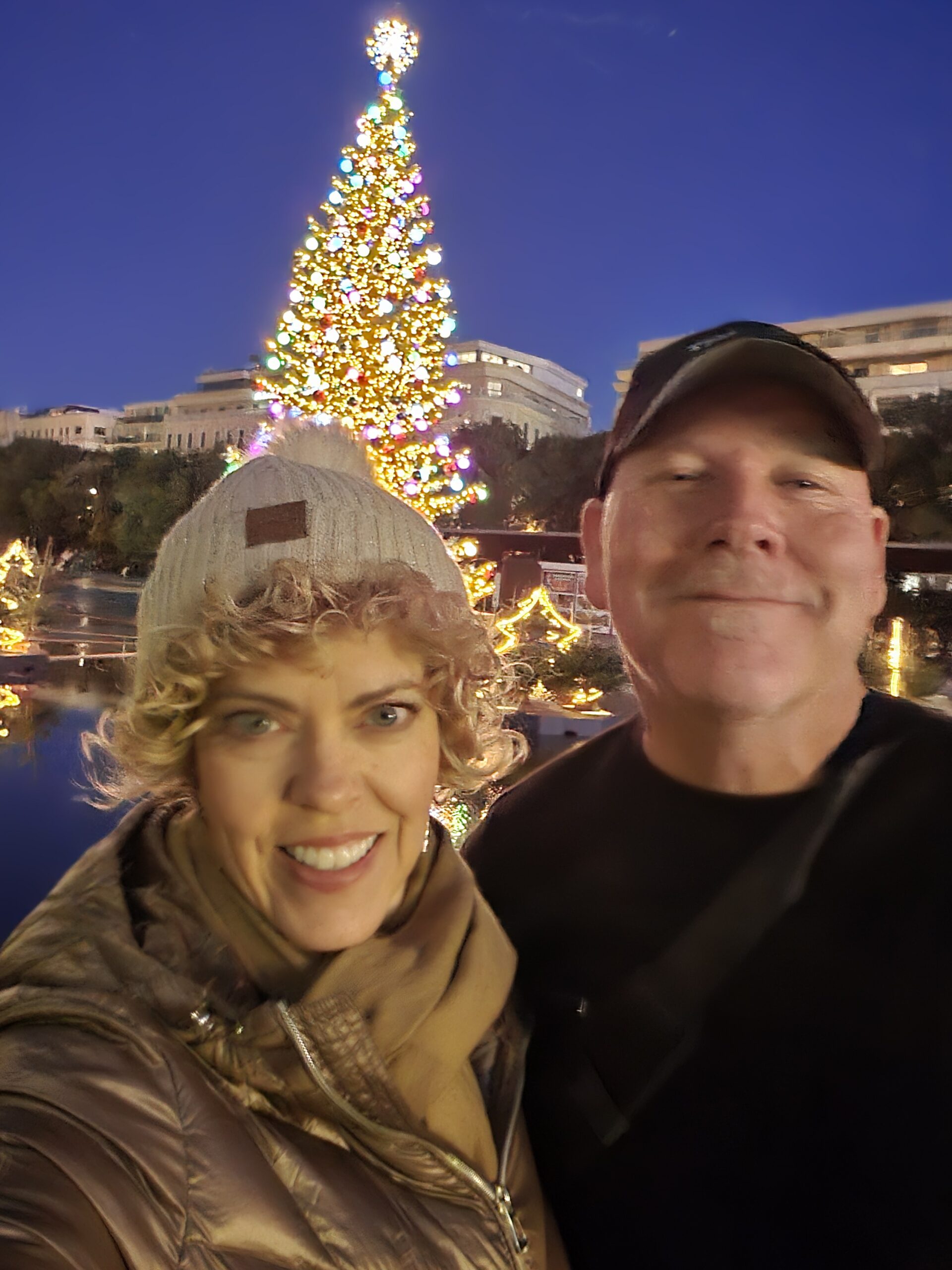 couple posing in front of a lit up Christmas tree outside; for blog post Christmas Market River Cruises in Germany and austria