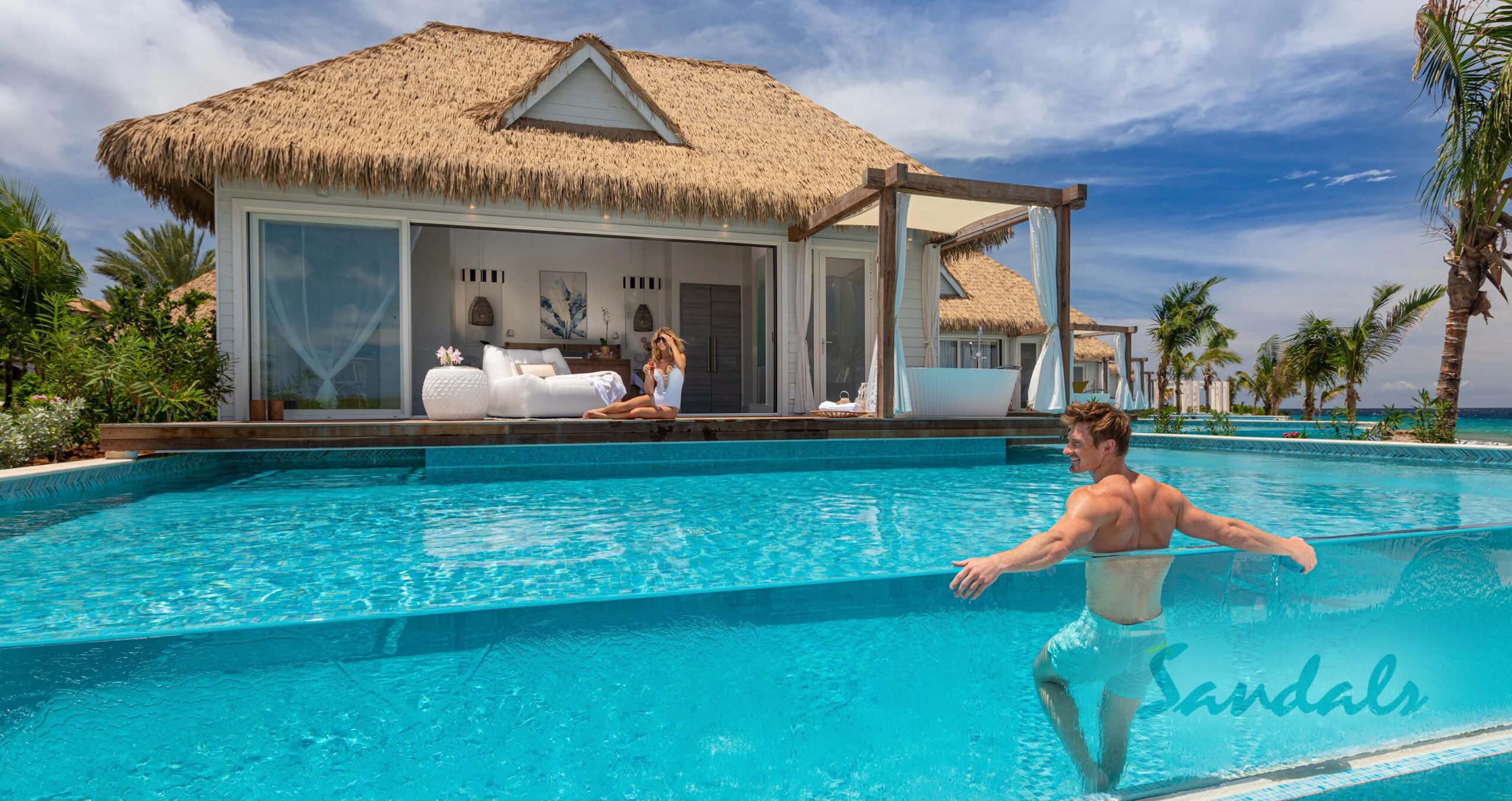 bungalow on the beach with a pool in front and a man sitting in the pool