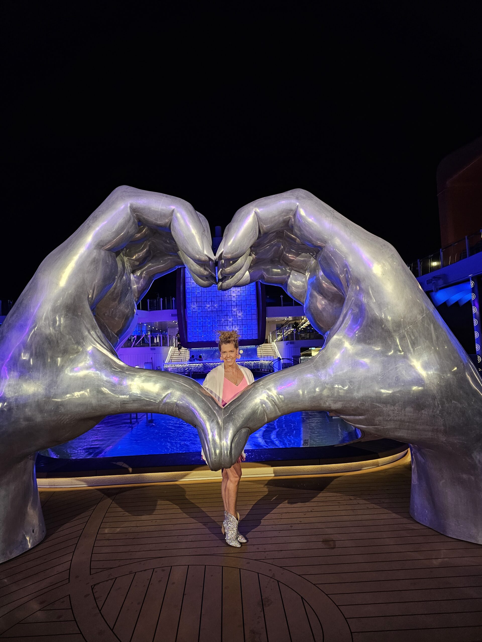 GG on Celebrity cruise ship standing inside a big art display of hands forming a heart. Cruise tips for first timers