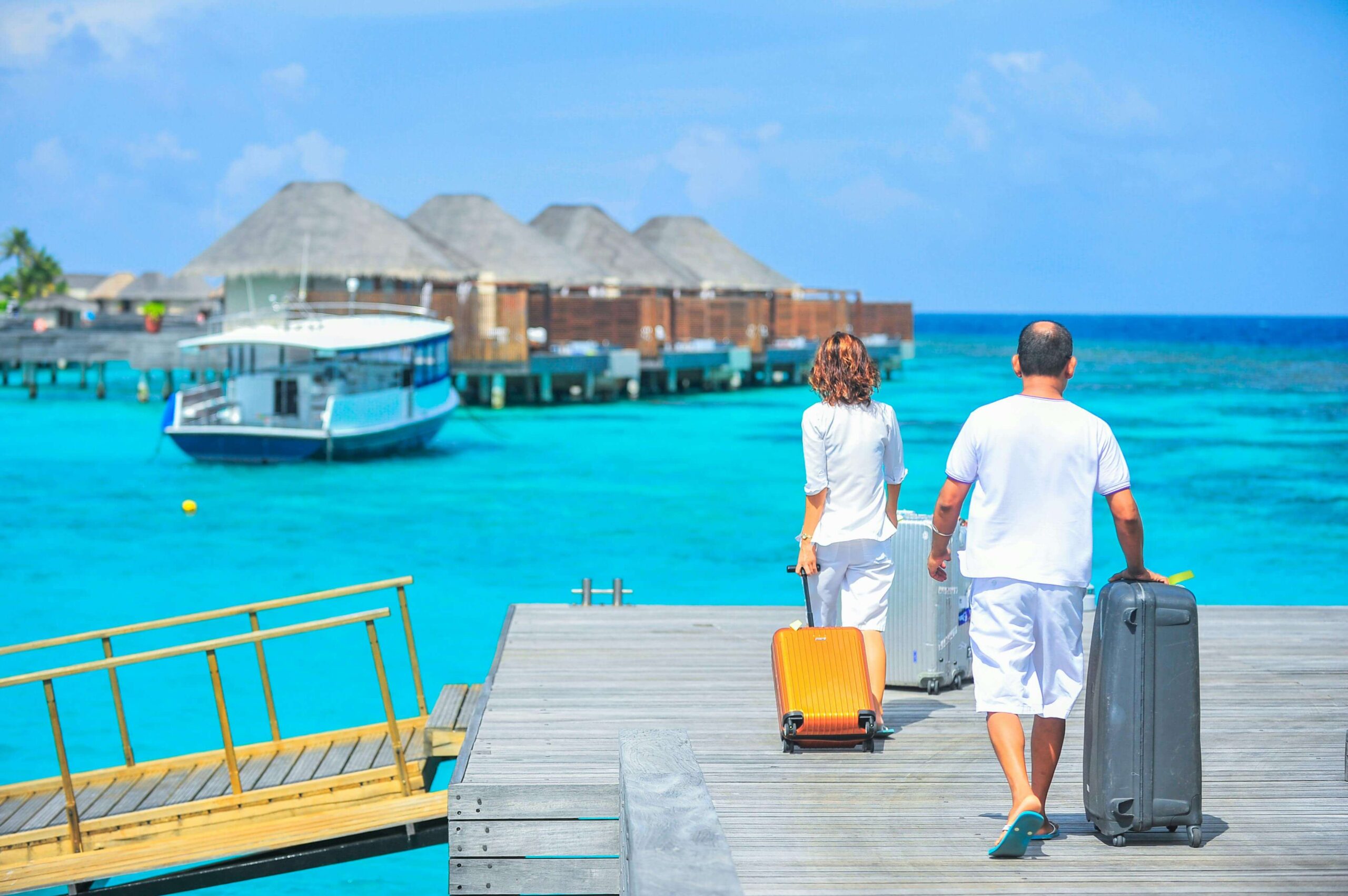 couple with luggage walking on dock towards overwater bungalows; from blog Stress free honeymoon planning