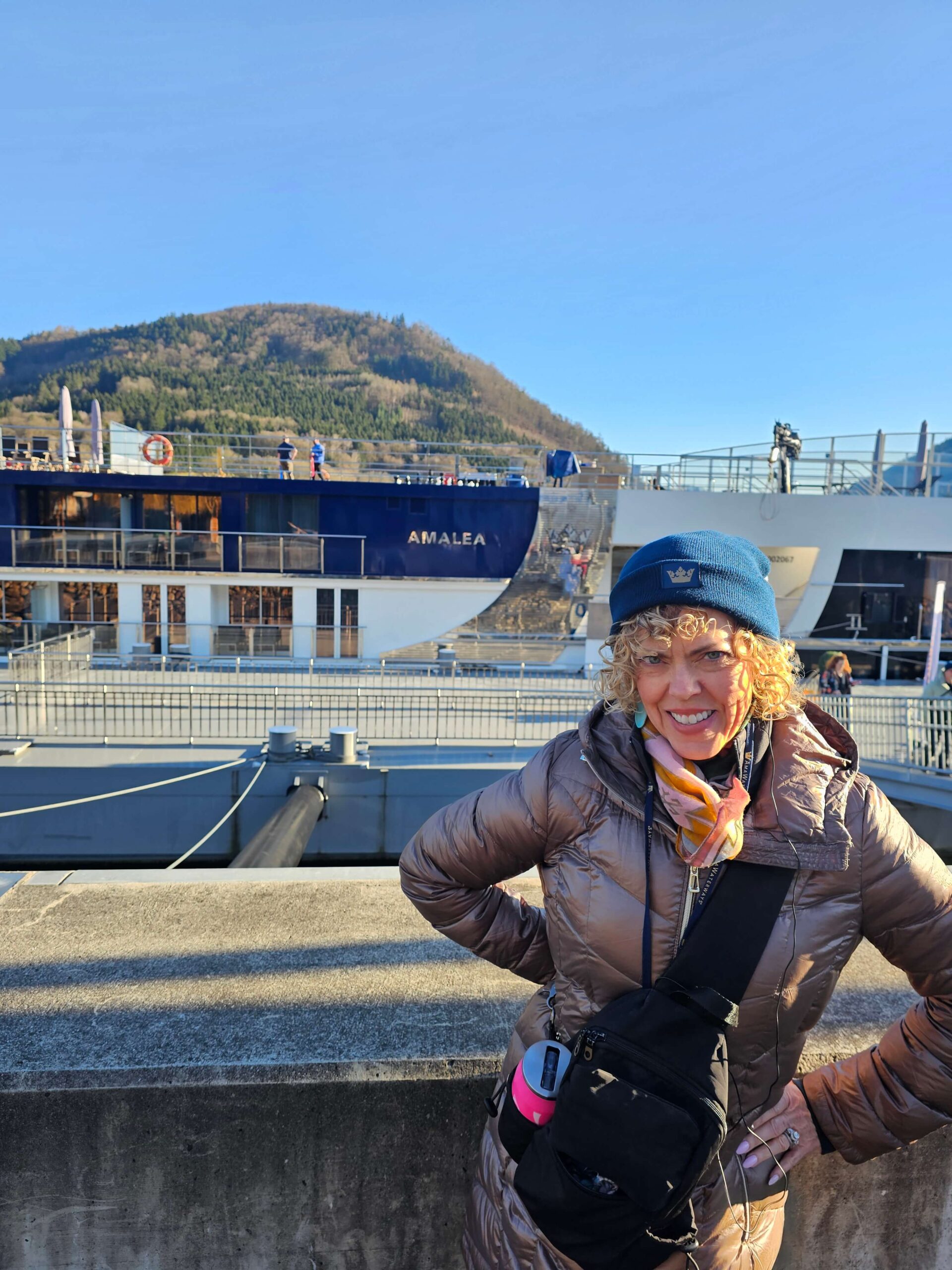 pciture of GG bundled up in coat and hat standing outside in front of rver cruise ship, AmaLea, small ship vs mega cruise blog post