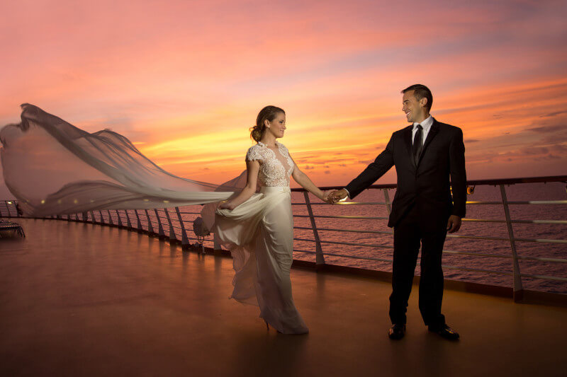 bride and groom onboard a ship with sun setting behind them. From blog post: why a cruise is the smart choice for your next wedding