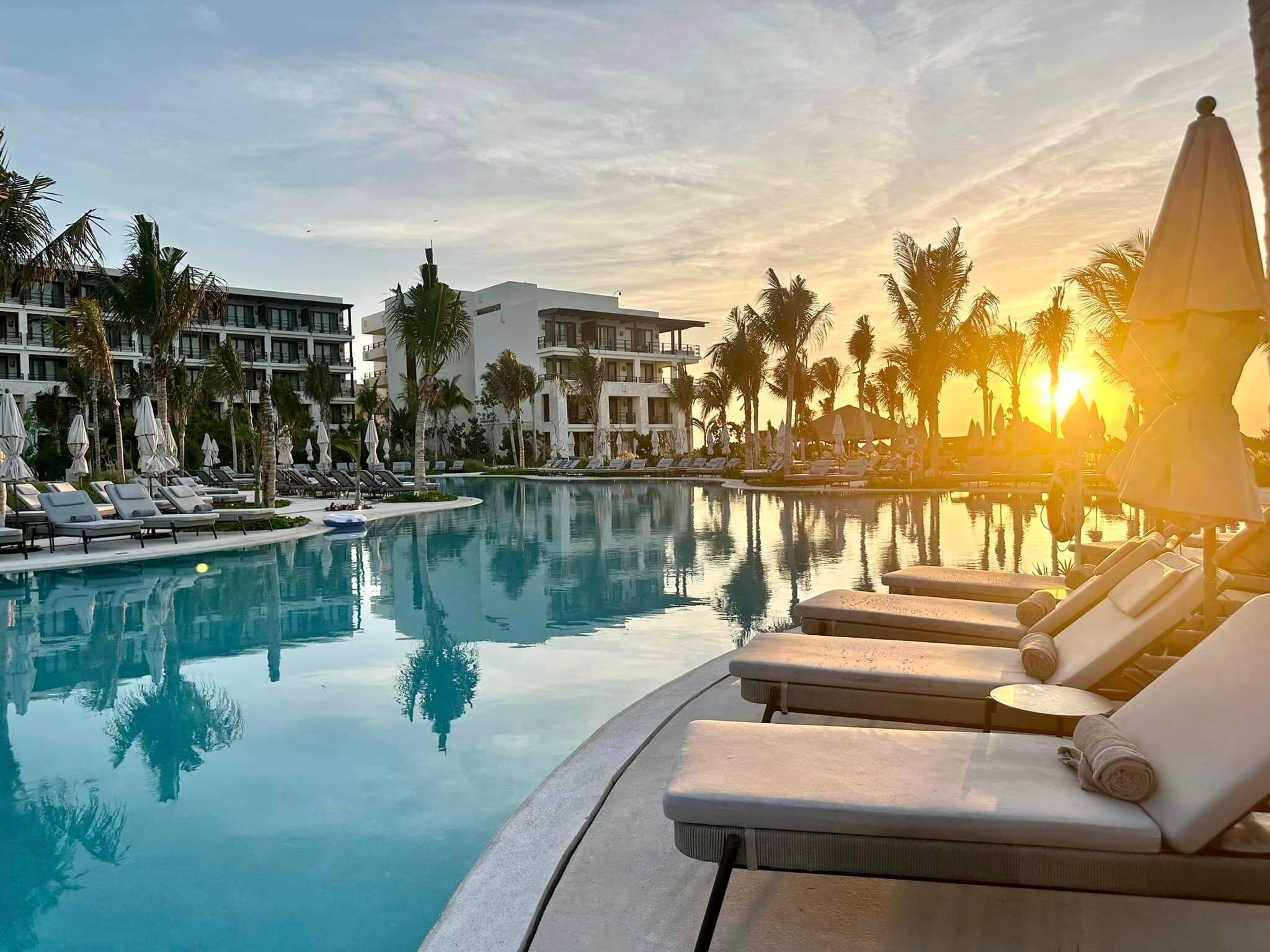 pool at sunset surrounded by lounge chairs and palm trees and a resort in the background; from blog post Black Friday All-Inclusive Resorts 2025