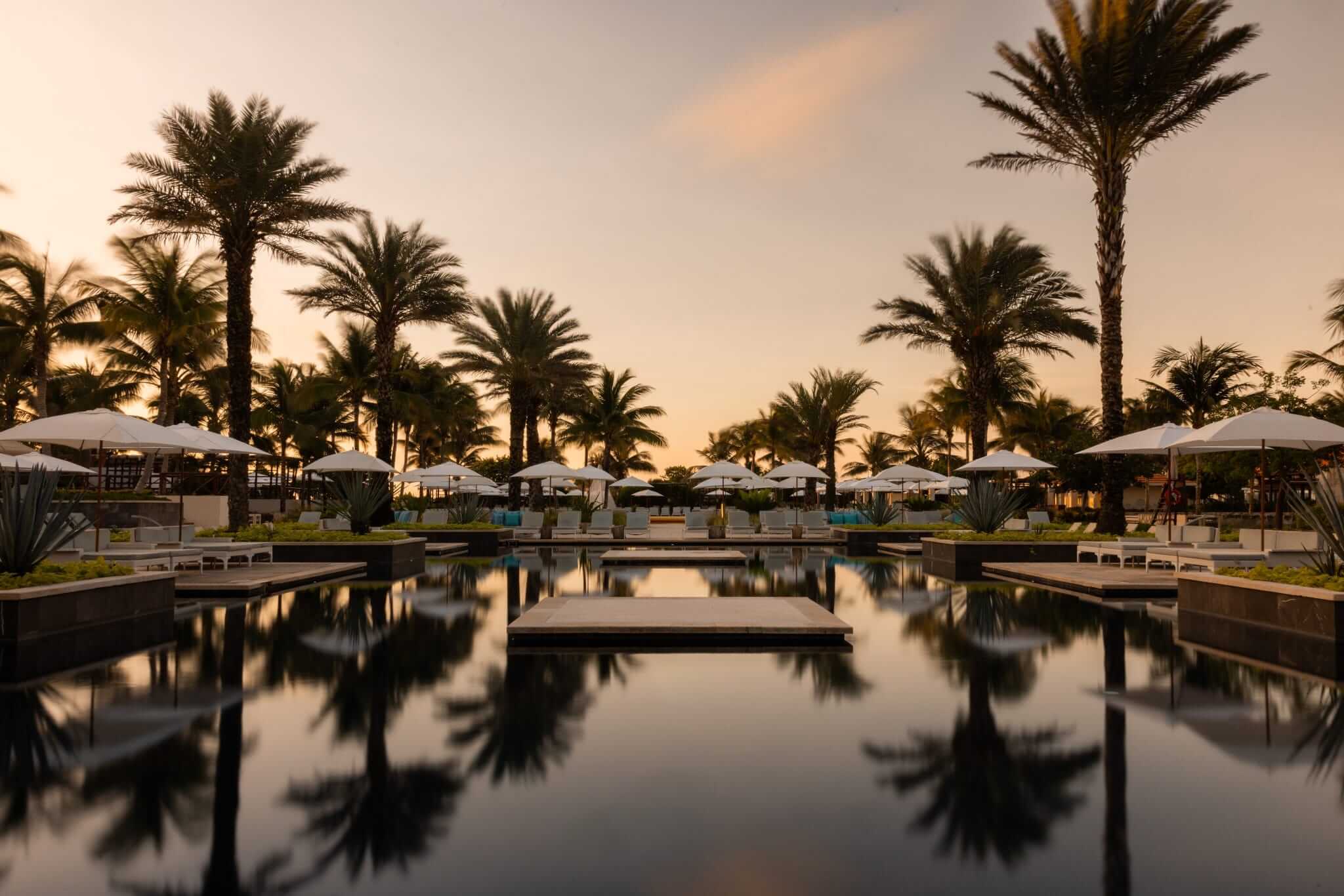 resort pool at sunset with palm trees and beach chairs surrounding it; from blog post: Black Friday All Inclusive Resort Specials