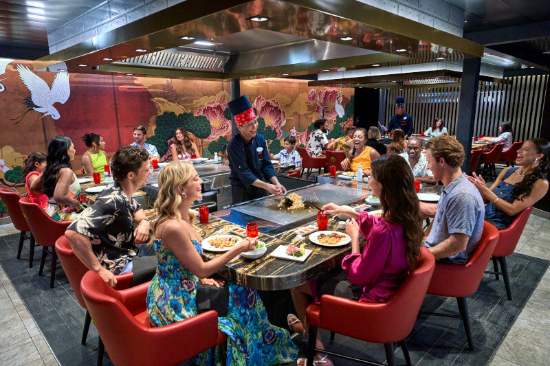 people sitting around a table while the chef cooks. From blog post: Utopia of the Seas honest review