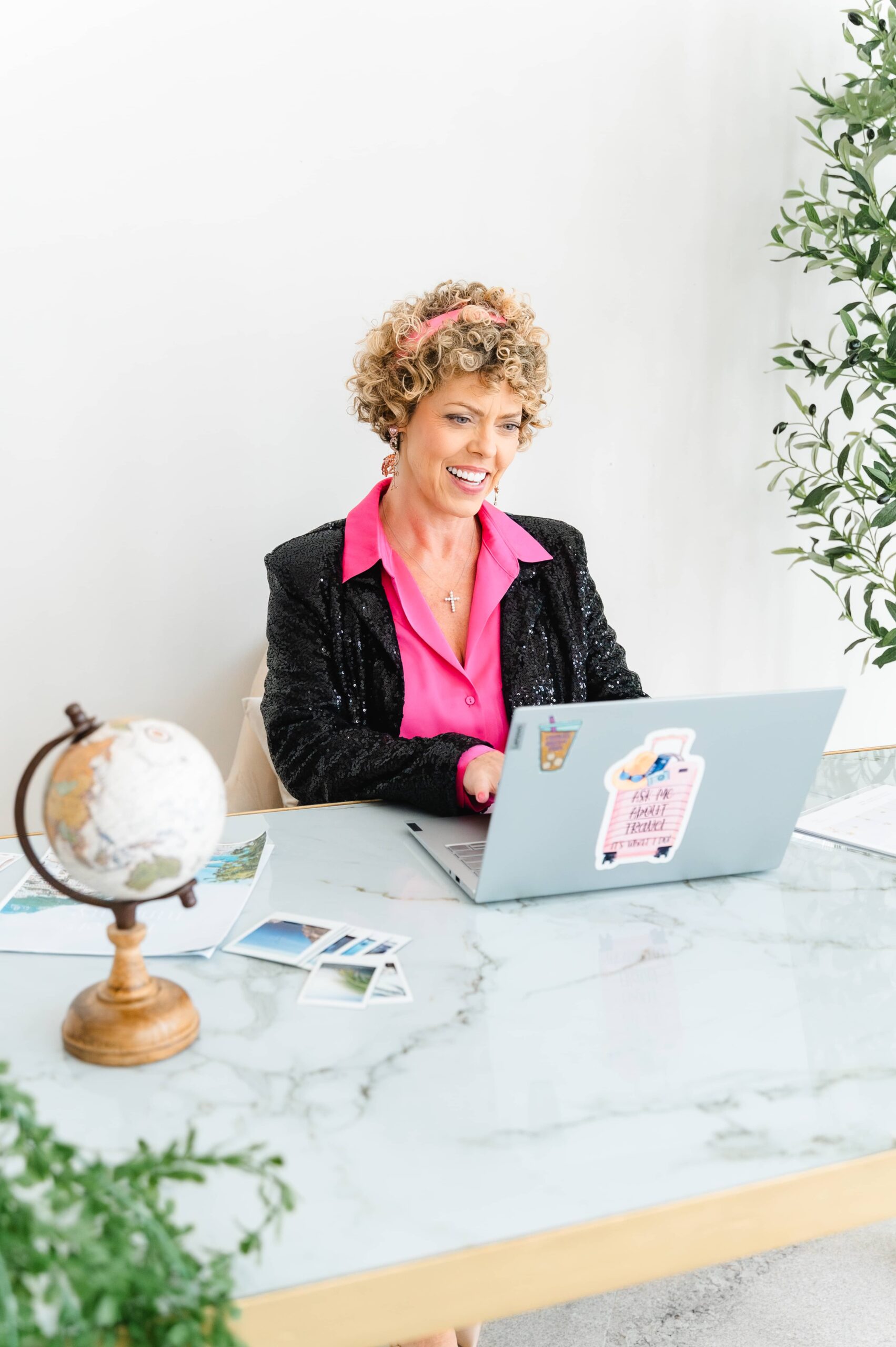 lady sitting at computer and desk wearing a pink shirt and black blazer from blog post Slow Travel for busy professionals