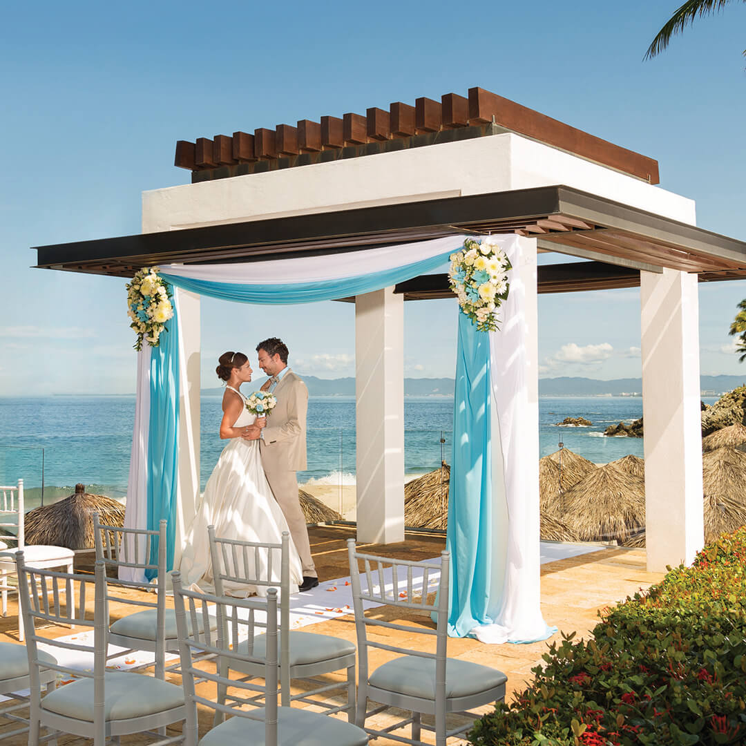 couple getting married on beach under a wedding arbor from blog post Micro Weddings 