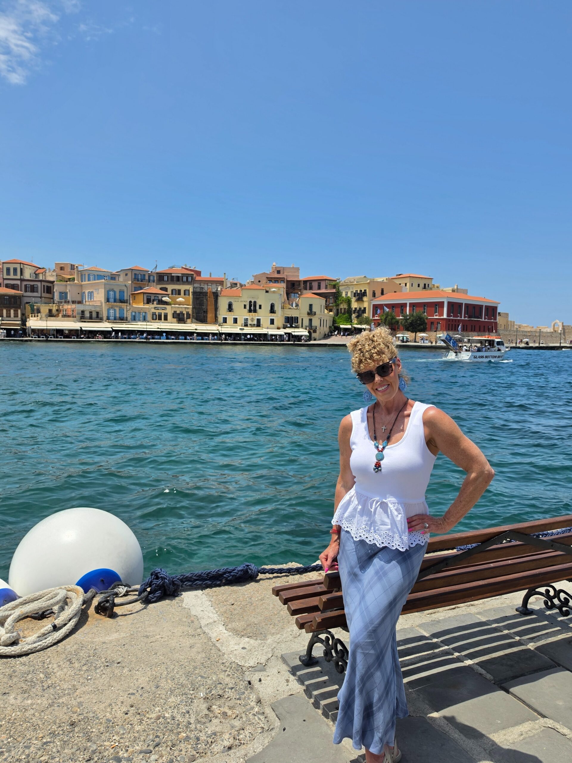 woman in white tank with long blue skirt standing by water with older european buildings in the background