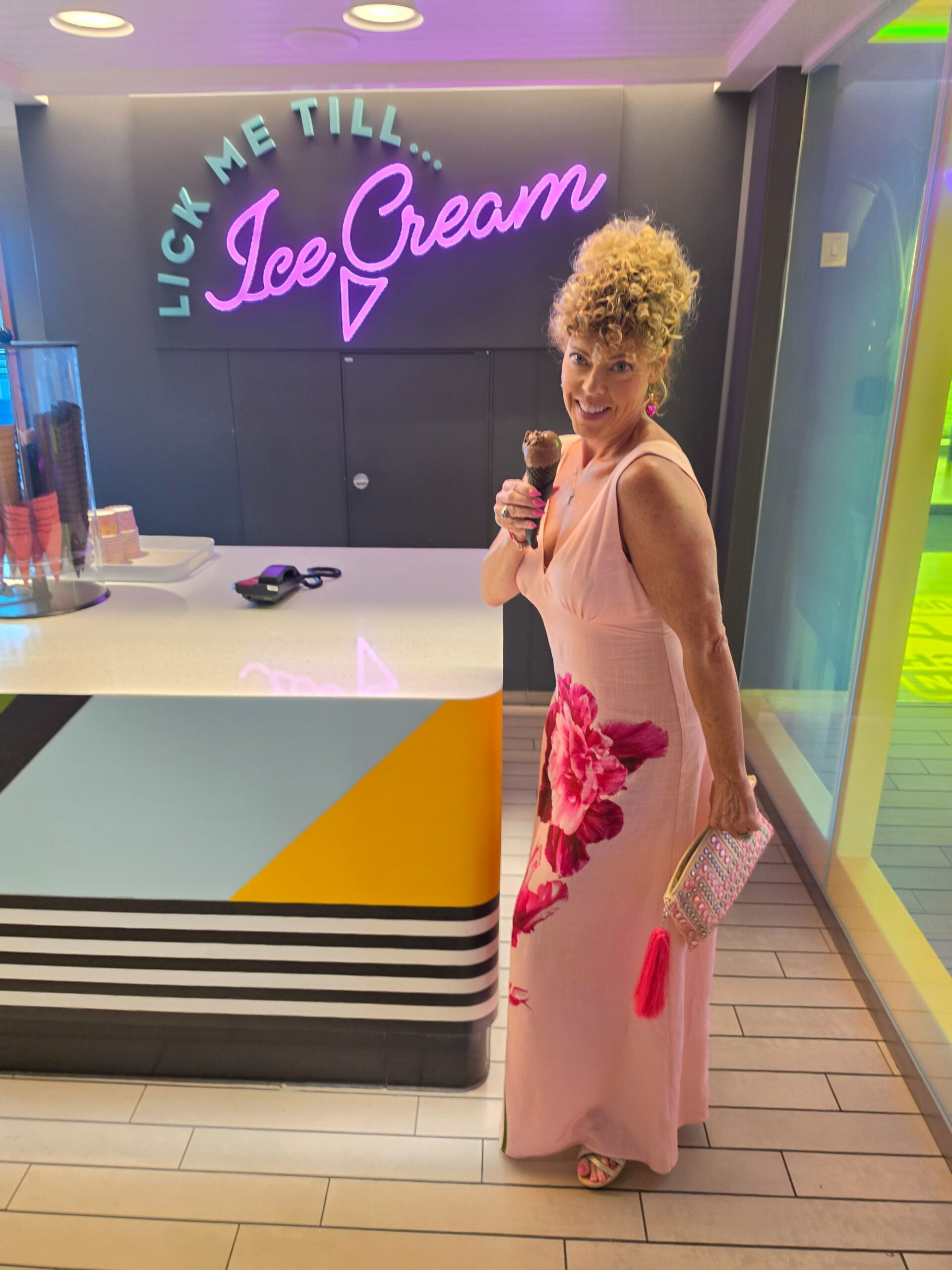girl in long pink sundress with ice cream cone in front of sign that says "lick me till ice cream"