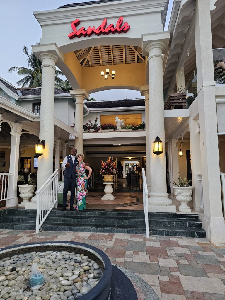 large plantation looking house with huge columns and a couple standing at the entrance with "Sandals" on the building from Sandals Royal Plantation resort