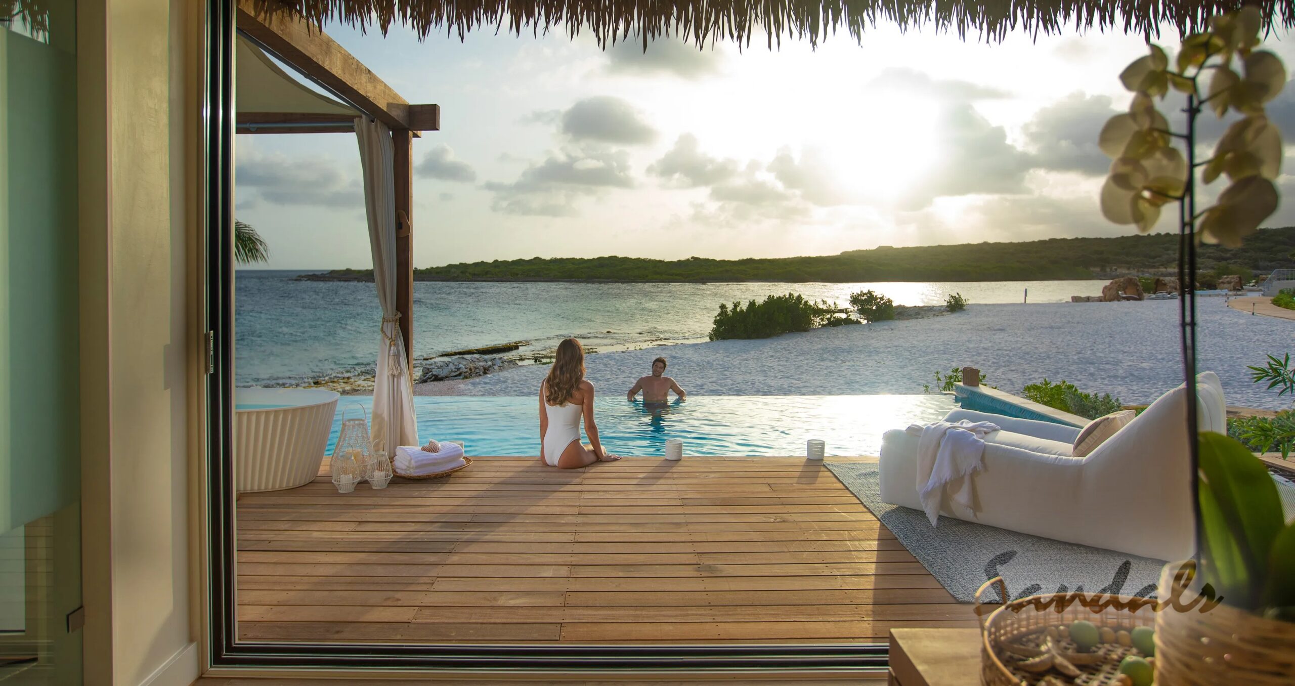 man sitting in a pool right on the beach while the woman sits on the deck looking at him.  This is at Sandals Curacao