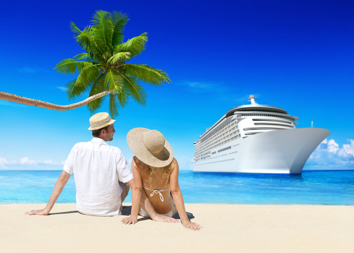 a couple laying in the sand on the beach looking at a cruise ship in the ocean