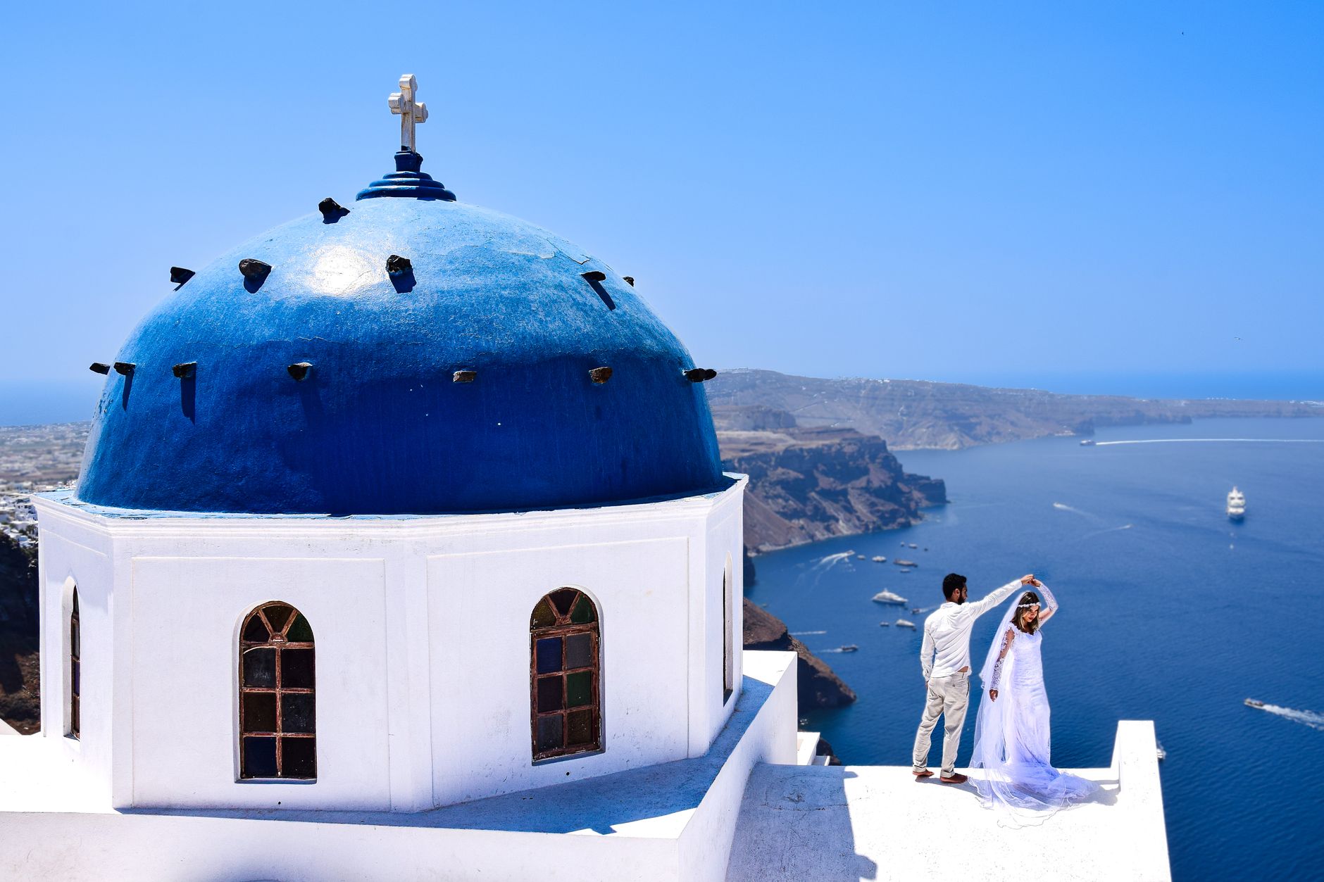 white church with blue dome and a wedding couple standing next to it overlooking the ocean
