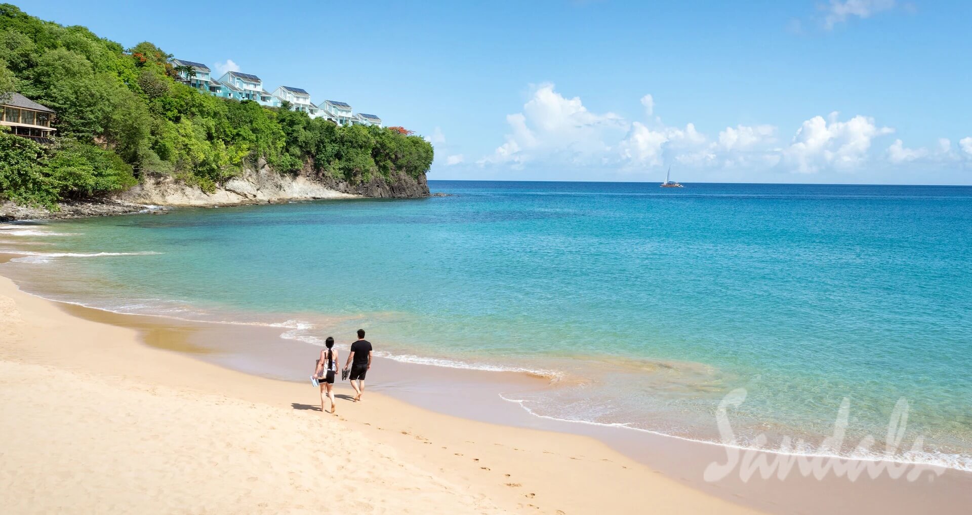 couple walking along the beach with a cliff in the front and resort rooms on the cliff at Sandals Regency La Toc